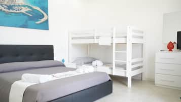Una camera d'albergo con un letto grande, un letto a castello, una cassettiera bianca e un quadro raffigurante una costa.