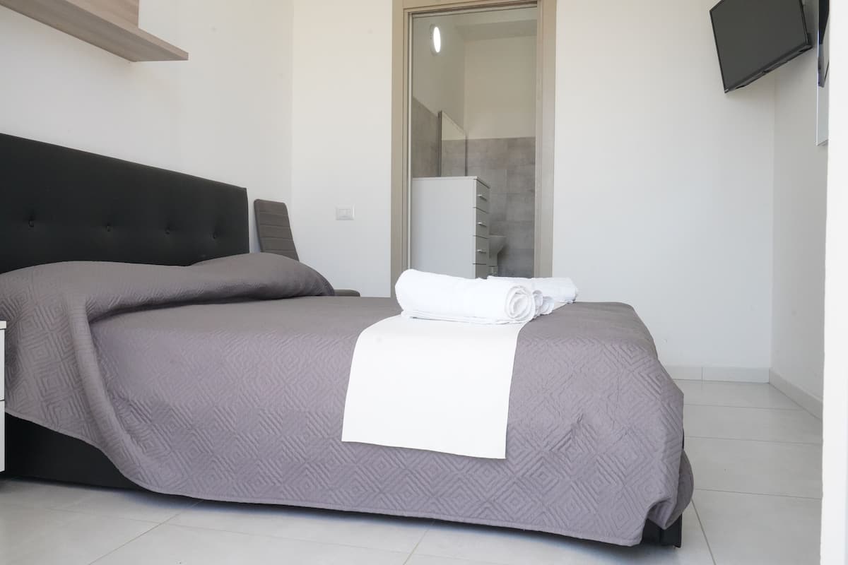 Una cama bien tendida con una colcha gris estampada y una toalla blanca encima.