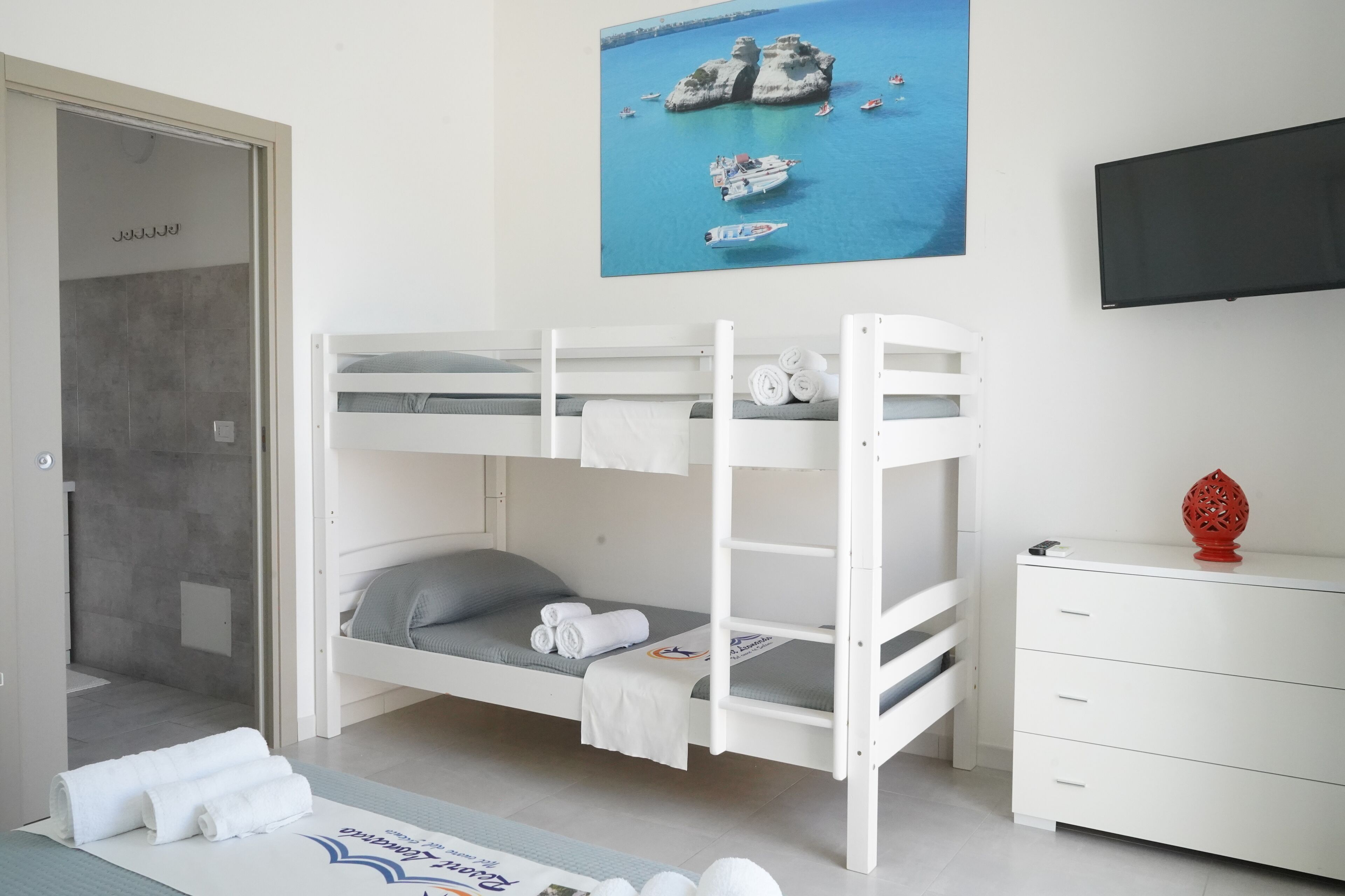 Dormitorio con literas y vistas al mar, un televisor y un aparador blanco.