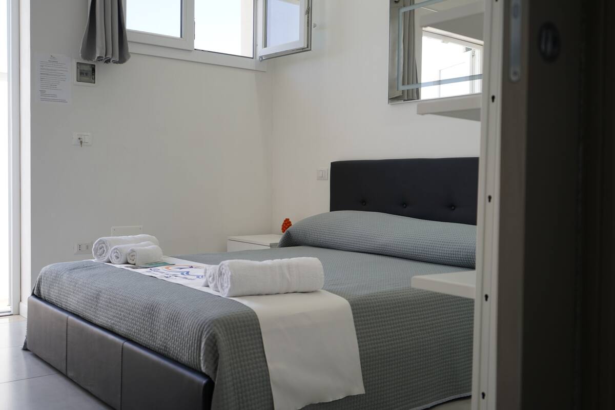Una habitación de hotel con una cama, una mesita de noche, un espejo y una ventana.