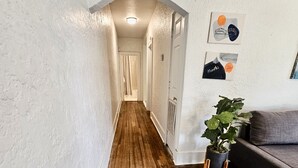 A narrow hallway with wooden flooring, white walls, and a gray couch with a blue patterned rug. - A cute fully furnished place in Midtown Memphis (Memphis)