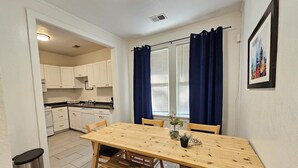 A compact kitchen with white cabinets, a wooden dining table with benches, and a small trash bin. - A cute fully furnished place in Midtown Memphis (Memphis)