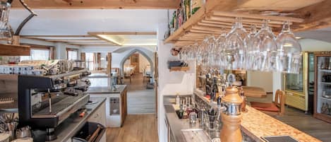 A bar area with espresso machines, a wooden counter, and a wine rack with glasses.