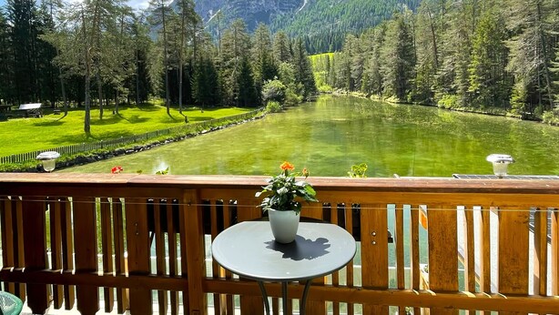 Una terraza de madera con una mesa y sillas, con vista a un paisaje verde con árboles y una montaña al fondo.