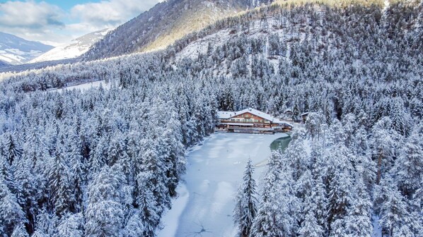 A snow-covered lodge surrounded by dense forest and mountains. - Hotel Lago della Creta (Marebbe)