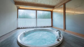 Un baño moderno con una bañera independiente, un amplio ventanal con vidrio esmerilado y vigas de madera en el techo.