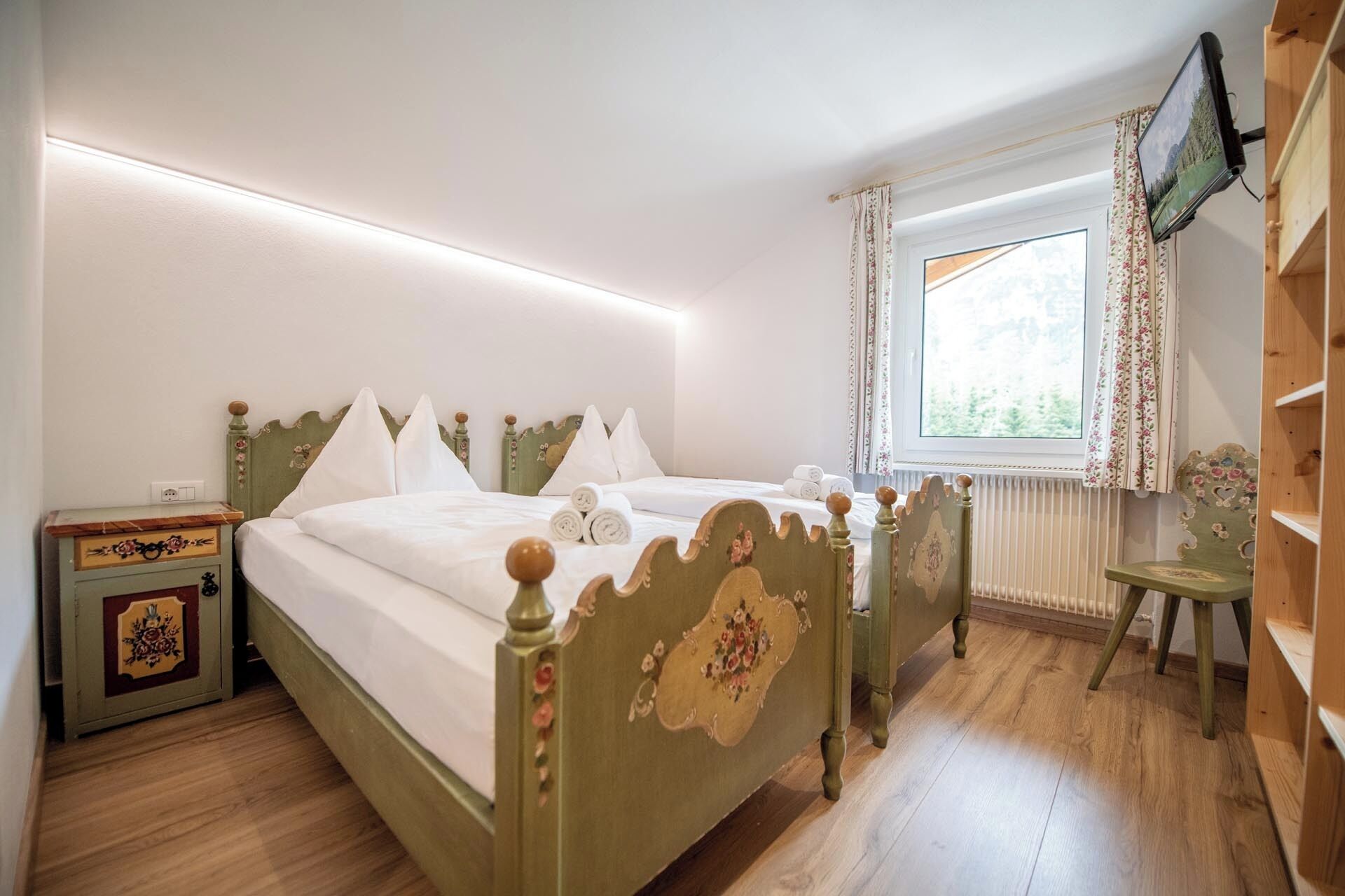 Une chambre à coucher avec un lit en bois, une table de chevet, une petite table et une fenêtre avec des rideaux.