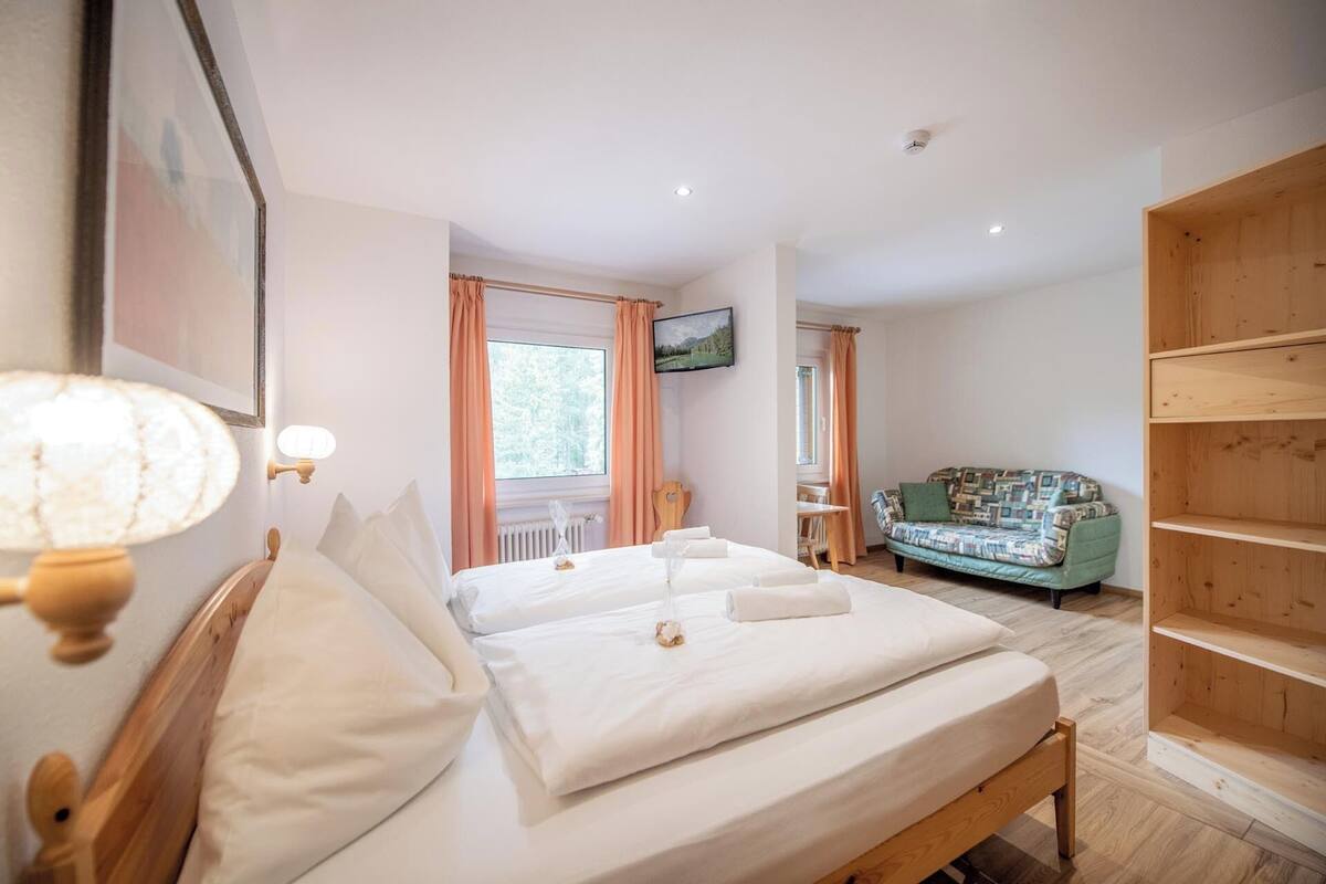 Un dormitorio con dos camas, un armario de madera, un televisor y una ventana con cortinas.
