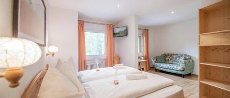 A bedroom with two beds, a wooden wardrobe, a television, and a window with curtains.
