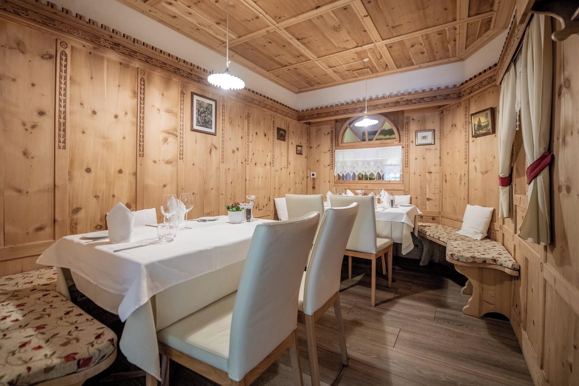 A wooden interior with a dining area, white chairs, and tables set for a meal.