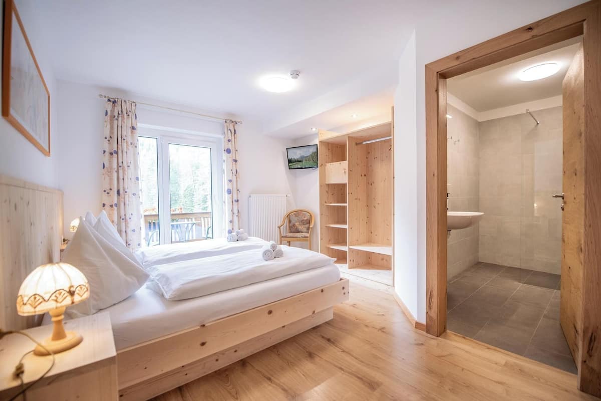 Un dormitorio con una cama, una lámpara de noche, una silla, un televisor y un armario de madera.