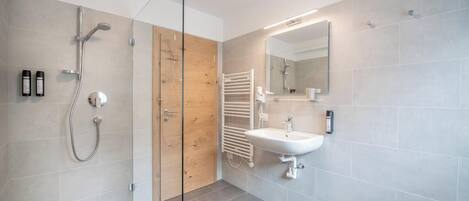 A modern bathroom with a glass shower enclosure, a wooden door, a white sink, and a mirror.