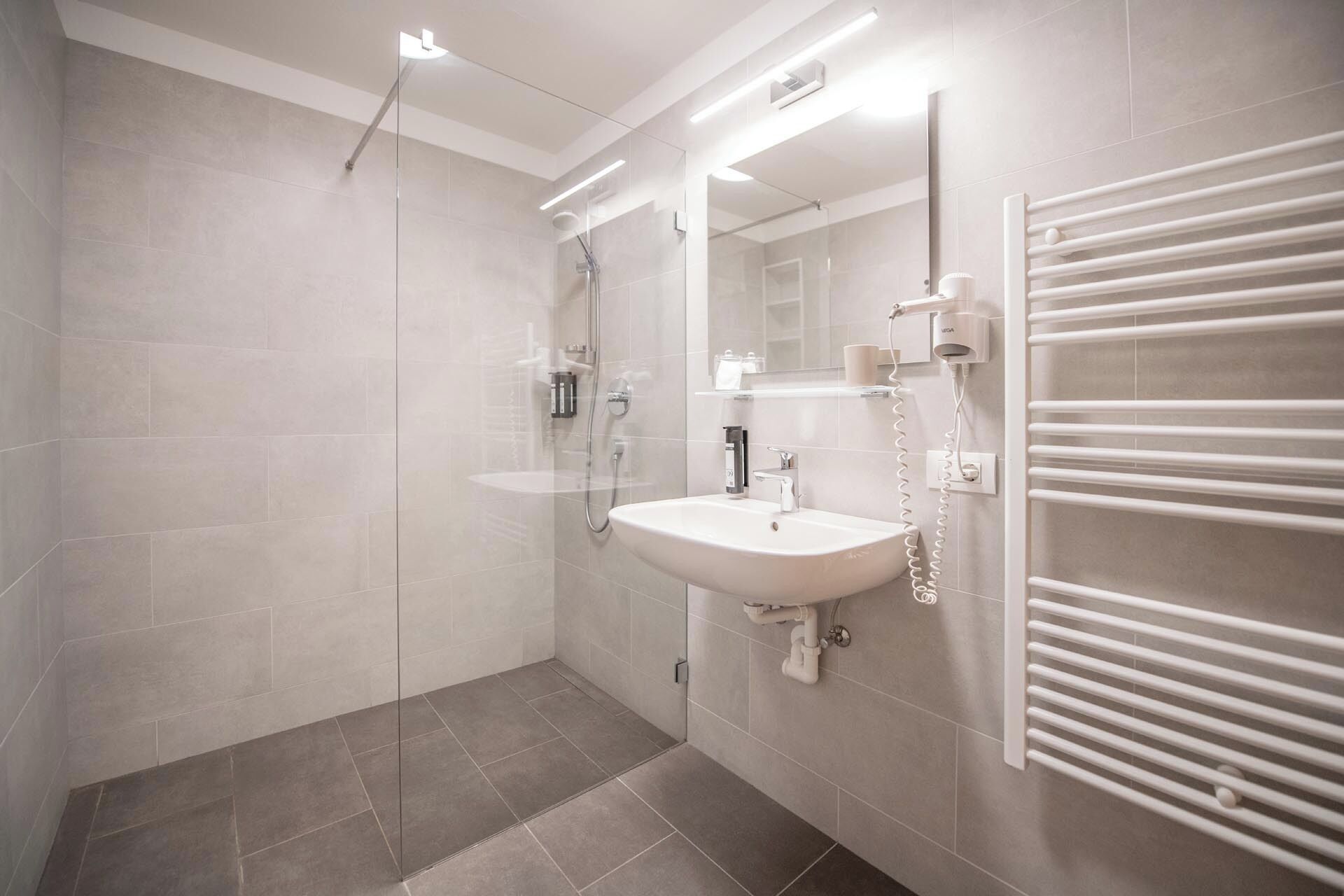 A modern bathroom with a glass shower enclosure, a white sink, and a towel rack.