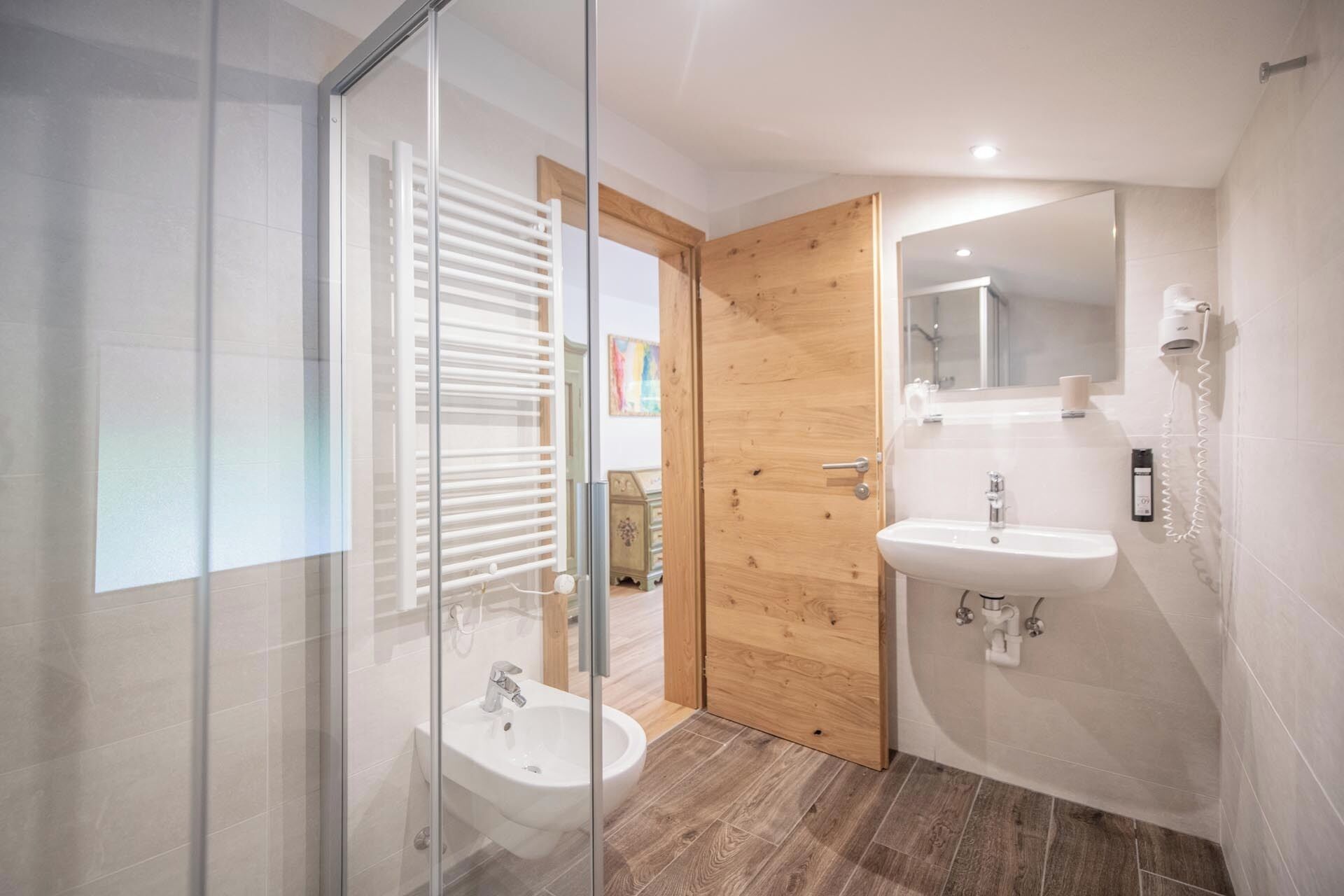 A modern bathroom with a glass shower enclosure, a wooden door, a sink, and a mirror.