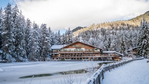 Un gran lodge con varios balcones, rodeado de árboles cubiertos de nieve y un lago congelado.