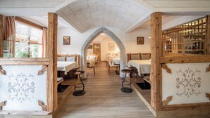 Un restaurante con un interior rústico, que presenta vigas de madera, arcos de piedra y una zona de comedor central con mesas y sillas.