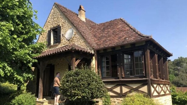 A stone house with a tiled roof, a wooden porch, and a small garden with flowers. - Gîte à la Campagne (Veyrignac)
