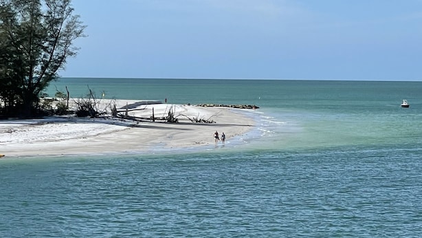 Ein Strand mit klarem türkisblauem Wasser, einem Sandufer und einigen Spaziergängern.