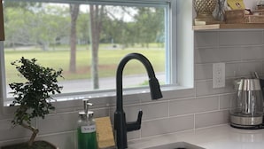Una cocina con un grifo negro, dispensador de jabón para platos, una esponja y una pequeña planta en maceta.