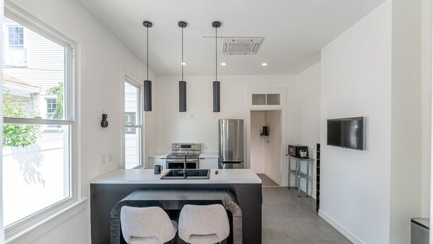 A modern kitchen with a central island, pendant lights, stainless steel appliances, and a TV mounted on the wall. - Legend RVA - Modern, Chic, Minimalist (Richmond)