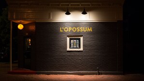 A building with a dark brick facade and the name 'L'OPOSSUM' in yellow letters. There is a small window with a stained glass design. - Legend RVA - Modern, Chic, Minimalist (Richmond)