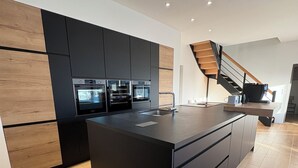 Una cocina moderna con una isla central, hornos integrados y una escalera de madera.