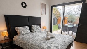 Un dormitorio con una cama grande, una mesita de noche con lámpara, una obra de arte en la pared y vistas al exterior a través de una puerta corredera.