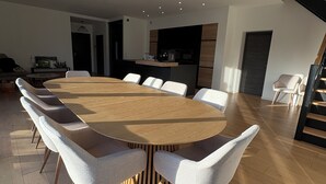 Un comedor moderno con una gran mesa redonda, seis sillas tapizadas y una cocina al fondo.
