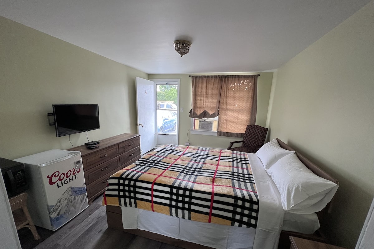 A bedroom with a bed, a dresser, a television, and a Coors Light cooler.