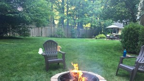 Un jardin avec un foyer en pierre, deux fauteuils Adirondack et une clôture en bois.