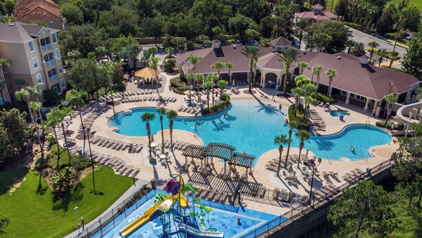 Luftaufnahme eines Resorts mit zwei Schwimmbecken, einem Wasserpark und umliegenden Palmen.