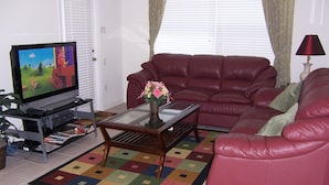 Ein Wohnzimmer mit Fernseher, einem roten Sofa, einem Couchtisch mit einer Vase und einem farbenfrohen Teppich.