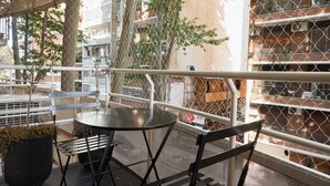 Un balcón con una mesa y sillas, una planta en maceta y vistas de un edificio de ladrillo con varios balcones.