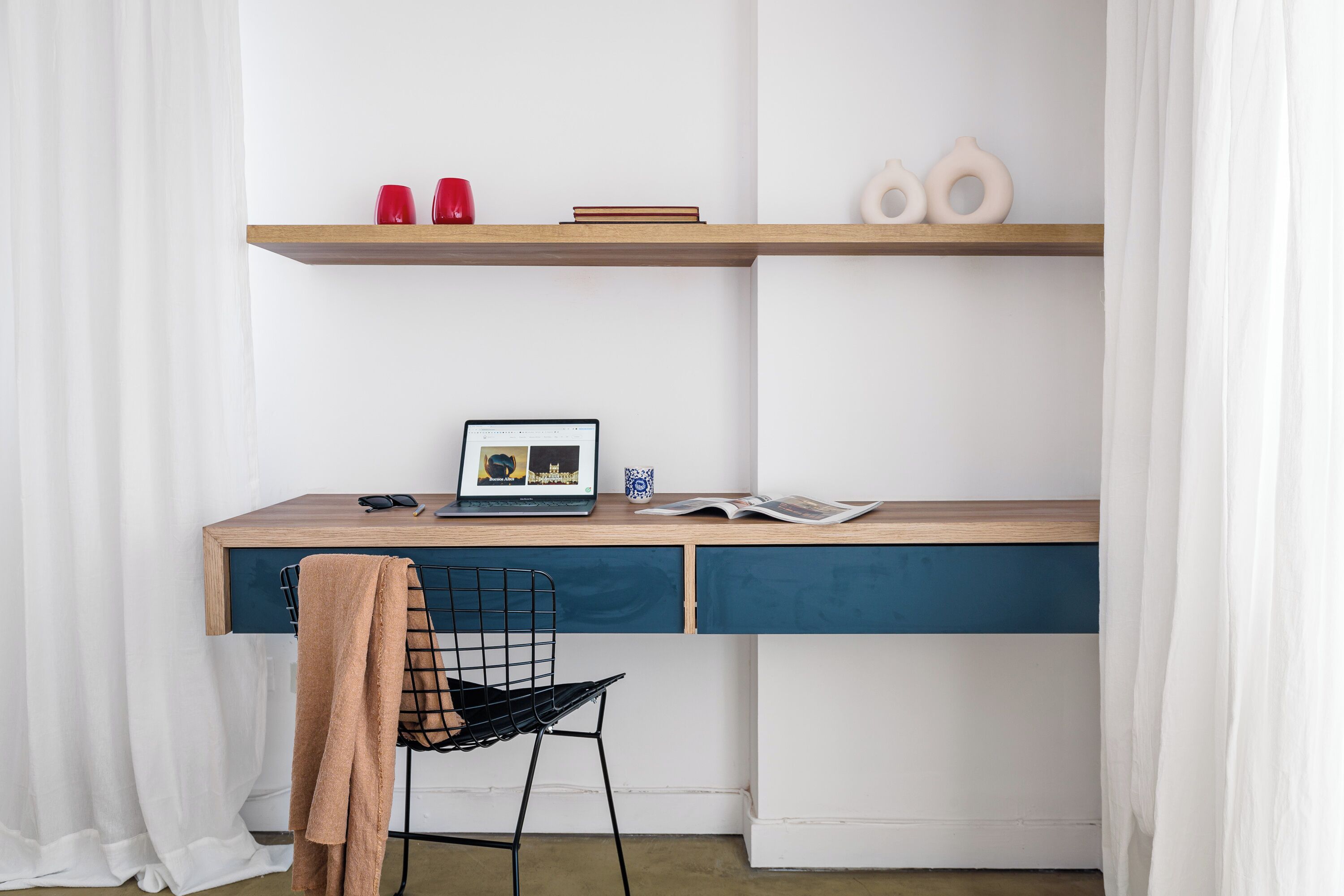 A study area with a wooden desk, a black chair, and a window with white curtains.