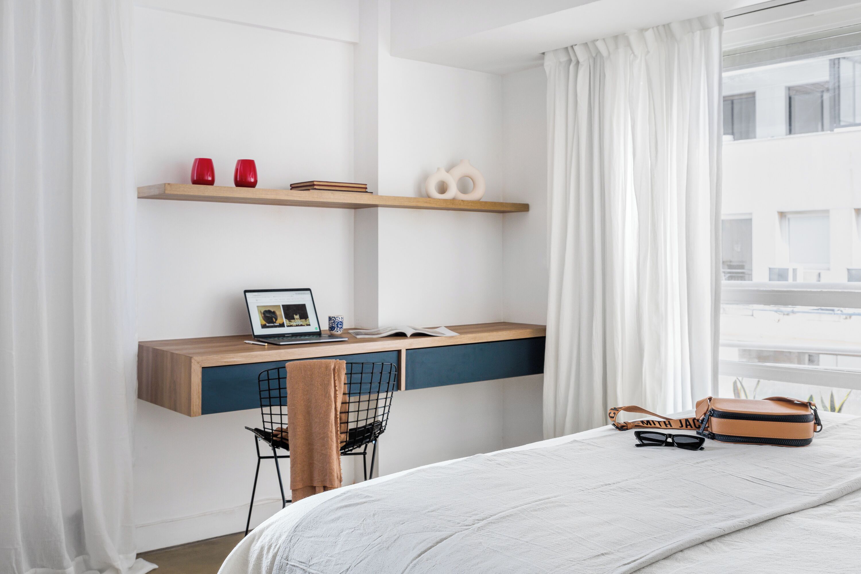 A modern bedroom with a wooden desk, a chair, a bed, and a window with curtains.