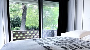 A bedroom with a large bed, a brick wall, and a window with a view of trees. - Studio Face Entrée de Roland Garros (BOULOGNE BILLANCOURT)