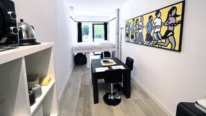 A compact hotel room with a bunk bed, a dining table with chairs, a kitchen area with a grill, and a large abstract painting on the wall. - Studio Face Entrée de Roland Garros (BOULOGNE BILLANCOURT)