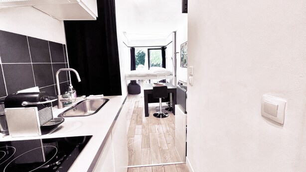 A modern kitchen with a black and white color scheme, a sink, a stove, and a window with a view of trees. - Studio Face Entrée de Roland Garros (BOULOGNE BILLANCOURT)