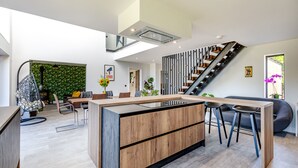 A modern kitchen with a central island, a dining area with chairs, a staircase, and a green wall. - 5 bedroom accommodation in Marldon, near Paignton (Marldon, near Paignton)