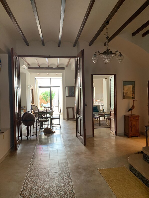 A spacious hallway with patterned tiles, wooden beams, and a chandelier.