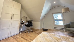 A bedroom with a sloped ceiling, a desk with a chair, a large wardrobe, a floor lamp, and a sofa. - Cozy 2-Bedroom Apartment In Historical Building.  (Grimsby)