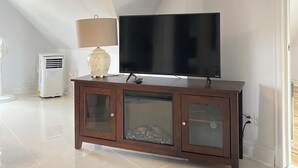 A modern living room with a flat-screen TV on a wooden cabinet, a standing fan, and a decorative vase. - Cozy 2-Bedroom Apartment In Historical Building.  (Grimsby)