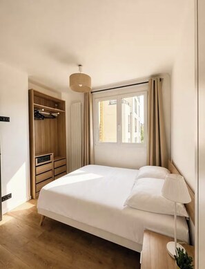 Ein Schlafzimmer mit Bett, Nachttischlampe, Kleiderschrank und Fenster.
