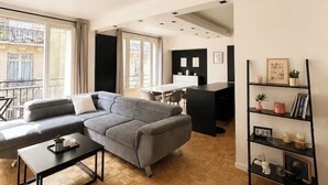 Een moderne woonkamer met een grijze bank, een bijzettafeltje en een zwarte boekenkast.