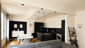 Een moderne woonruimte met een grijze modulaire bank, een eethoek en een keuken met zwarte kastjes.