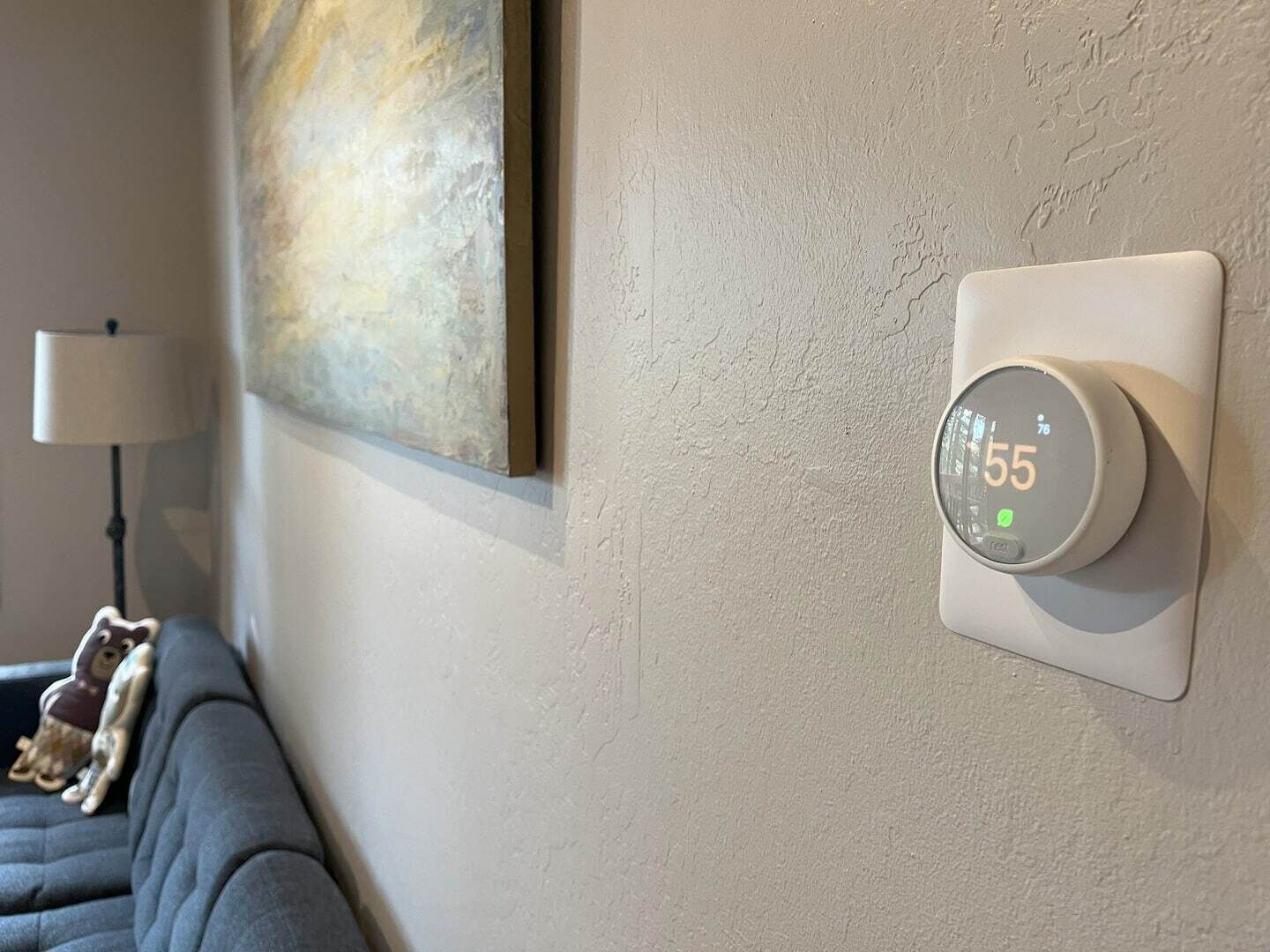 Een thermostaat aan de muur, een lamp en een bank met een decoratief object.