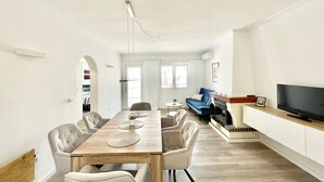 Ein geräumiges Wohnzimmer mit Esstisch aus Holz, gemütlicher Sitzgelegenheit, einem blauen Sofa und einem Flachbildfernseher.