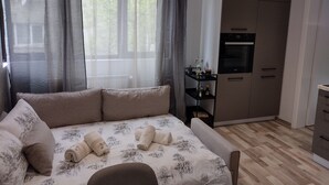 Un dormitorio con cama, una kitchenette pequeña y vistas a árboles a través de cortinas translúcidas.