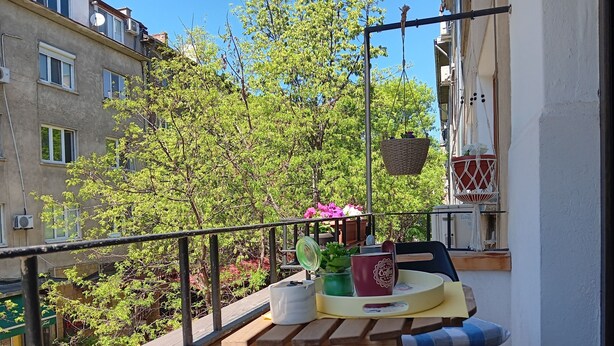 Un balcón con una mesa de madera, dos sillas, una cesta colgante y una planta en maceta.