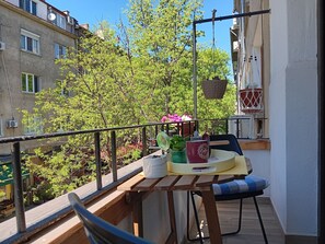 A balcony with a wooden table, two chairs, a hanging basket, and a potted plant. - Bijoux Apt: Comfort and Style in the heart of Sofia (Sofia)